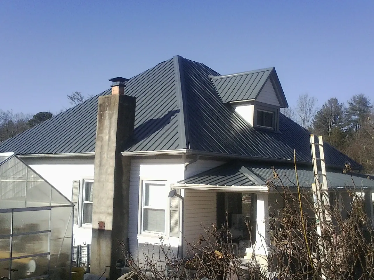 Dark blue standing seam metal roof on a white farmhouse with dormer — Slate & Tile Roof Repair by Roofing Brothers in Swan Lake