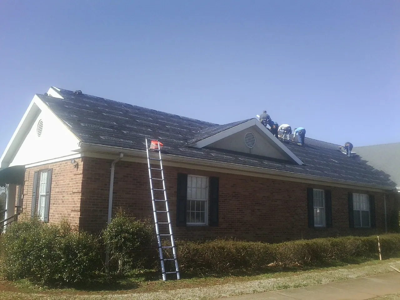 Crew tearing shingles off a brick ranch roof with a ladder set — Metal Roof Repair work by our crew in Swan Lake