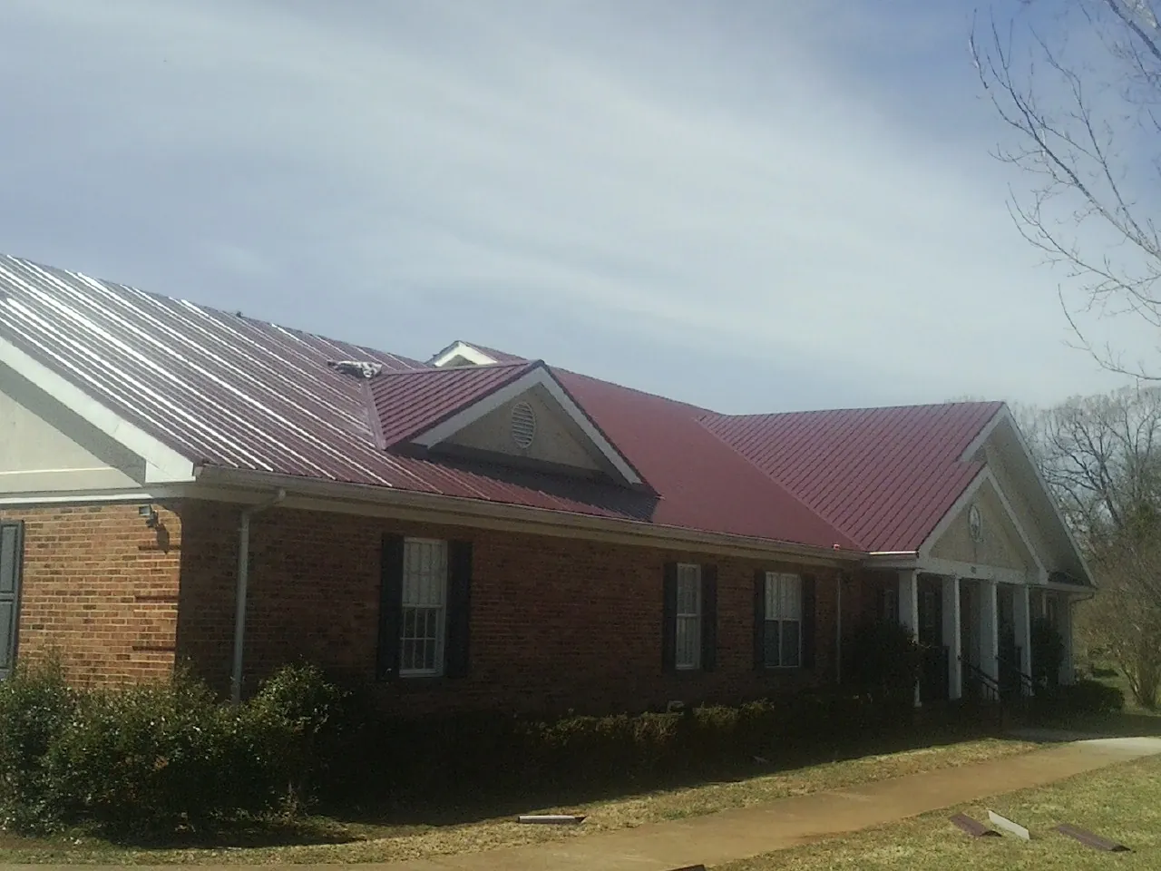 Red metal roof with gabled entries on a long brick building, from a Hail Damage Roof Repair job in Swan Lake