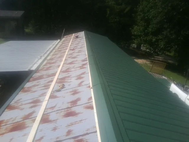 Old rusted panels beside newly installed green metal roofing — Wind Damage Roof Repair by Roofing Brothers in Swan Lake