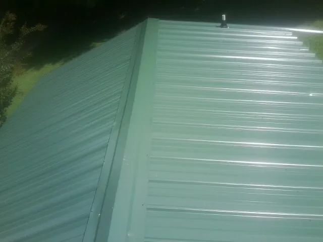 New green metal panels meeting at the ridge of a roof — Flat Roof Repair work by our crew in Swan Lake