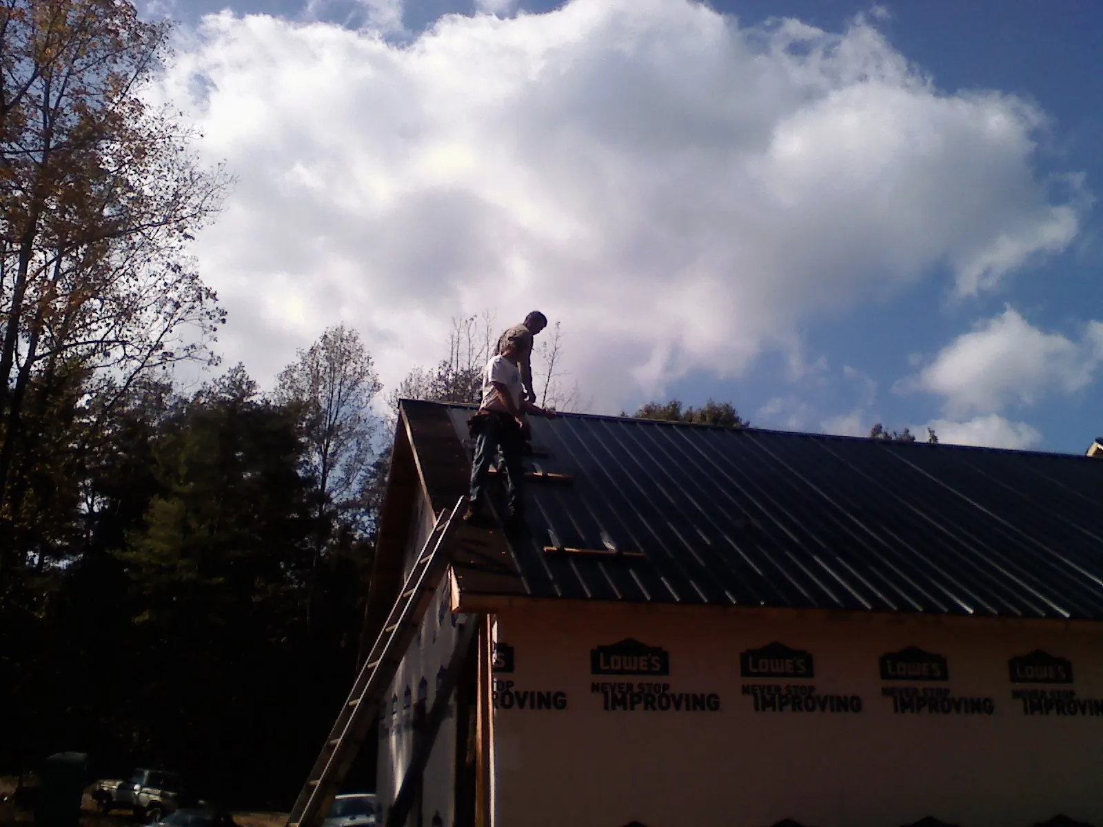 Roofer fastening dark metal panels high against a cloudy sky, from a Roof Inspection job in Swan Lake