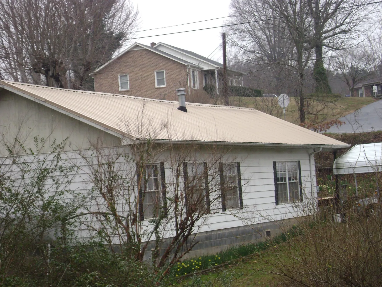 Tan metal roof on a white sided house set into a hillside — Commercial Roofing by Roofing Brothers in Swan Lake