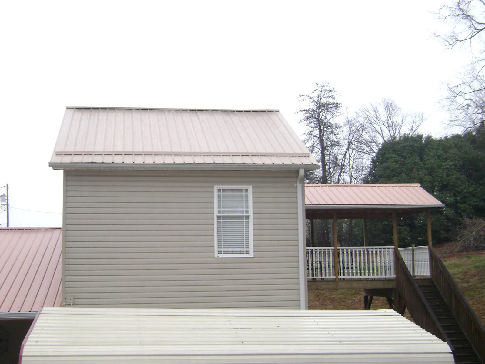 Tan metal roofs on a two story addition and attached porch, from a Roof Replacement job in Swan Lake